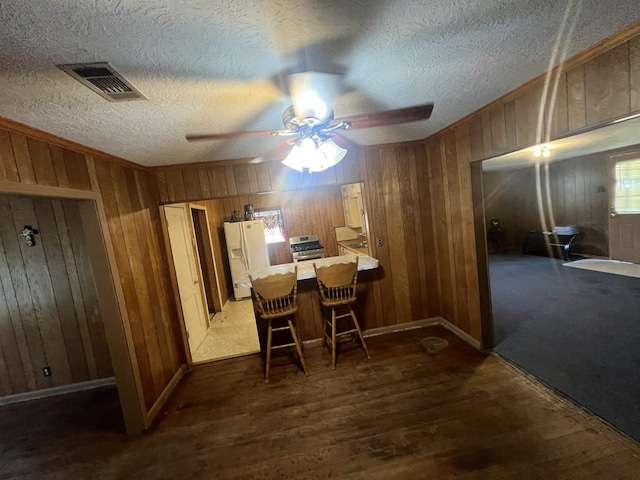 dining room featuring ceiling fan, dark wood-type flooring, and wood walls