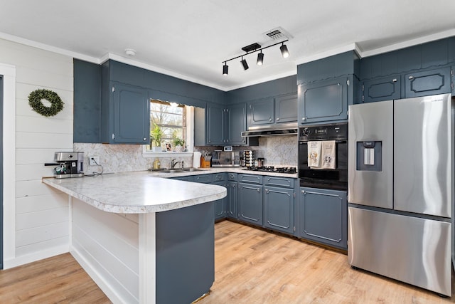 kitchen with light wood finished floors, under cabinet range hood, light countertops, a peninsula, and black appliances