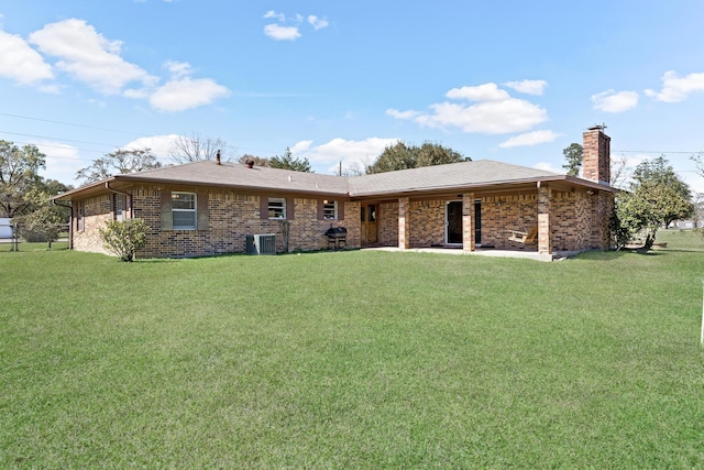 back of property with a yard, a chimney, brick siding, and central AC