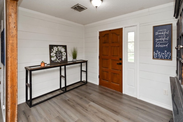 foyer with a textured ceiling, dark hardwood / wood-style floors, ornamental molding, and wood walls