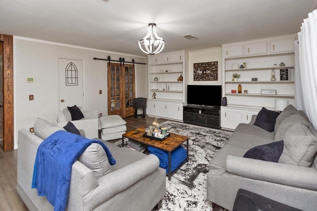 living room with a barn door, crown molding, an inviting chandelier, and light wood-type flooring