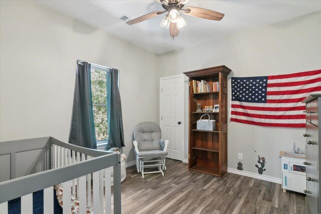 bedroom with ceiling fan, dark wood-type flooring, and a nursery area