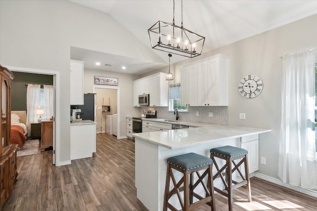 kitchen with pendant lighting, lofted ceiling, kitchen peninsula, appliances with stainless steel finishes, and white cabinetry