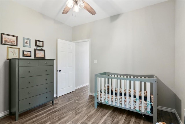 bedroom with a crib, hardwood / wood-style floors, and ceiling fan