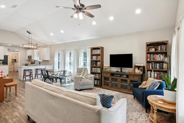 living room with ceiling fan with notable chandelier, sink, light hardwood / wood-style flooring, and vaulted ceiling