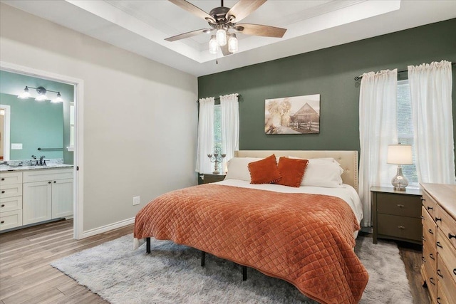 bedroom with ceiling fan, sink, a raised ceiling, ensuite bathroom, and light wood-type flooring