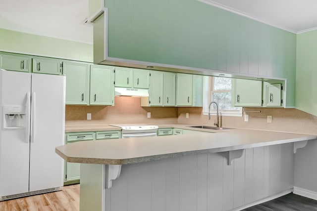 kitchen with kitchen peninsula, a kitchen bar, white appliances, sink, and green cabinetry