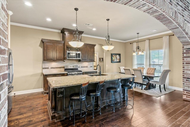 kitchen with sink, light stone counters, a kitchen bar, a center island with sink, and appliances with stainless steel finishes