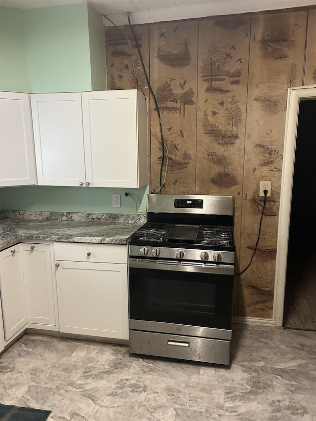 kitchen featuring wood walls, white cabinets, dark stone counters, and stainless steel range with gas stovetop