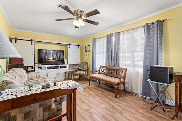 living room with a barn door, ornamental molding, a ceiling fan, and light wood finished floors