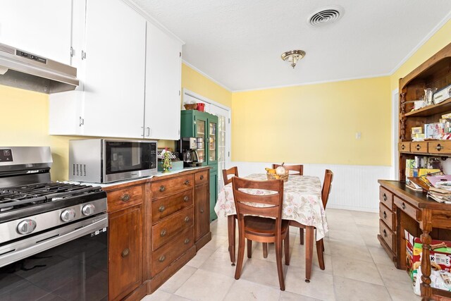 kitchen featuring wainscoting, stainless steel appliances, under cabinet range hood, ornamental molding, and visible vents