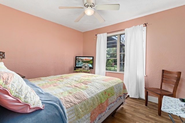 bedroom featuring a ceiling fan, a textured wall, wood finished floors, and baseboards