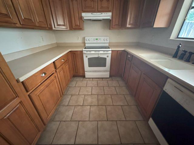 2985 Willow Pl, Beaumont, TX 77707 - kitchen featuring white appliances, under cabinet range hood, light countertops, brown cabinetry, and light tile patterned floors