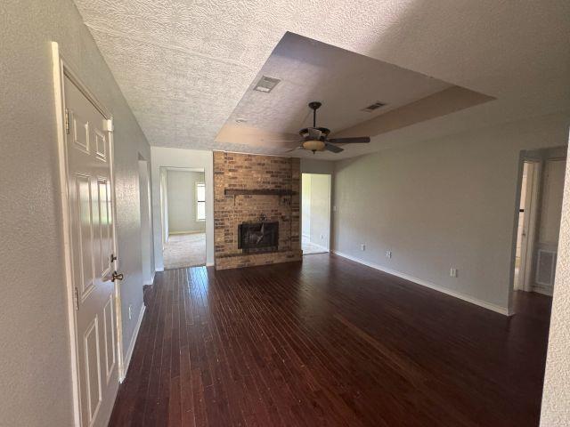 2985 Willow Pl, Beaumont, TX 77707 - unfurnished living room featuring hardwood / wood-style flooring, ceiling fan, a fireplace, and a textured ceiling