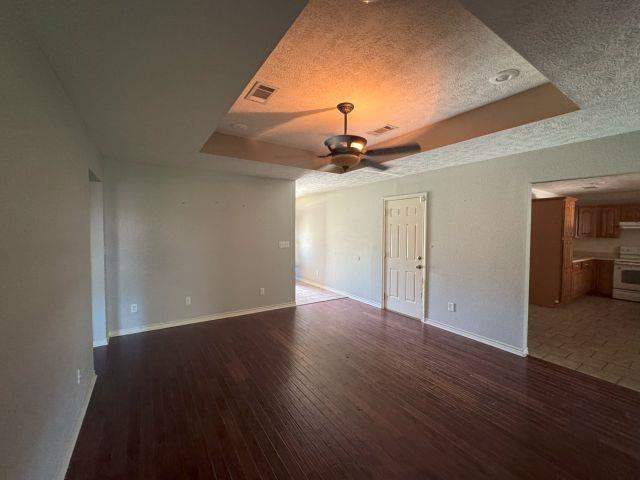2985 Willow Pl, Beaumont, TX 77707 - empty room with a tray ceiling, wood-type flooring, a ceiling fan, and a textured ceiling