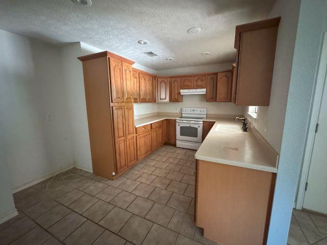 2985 Willow Pl, Beaumont, TX 77707 - kitchen featuring electric range, under cabinet range hood, light countertops, a textured ceiling, and light tile patterned floors