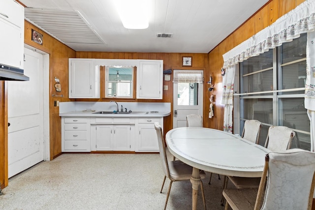 kitchen featuring a sink, light countertops, white cabinetry, wooden walls, and light flooring