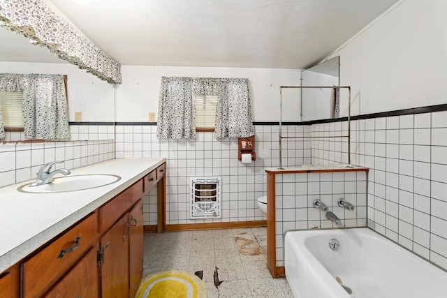 bathroom with heating unit, tile walls, toilet, a tub to relax in, and vanity