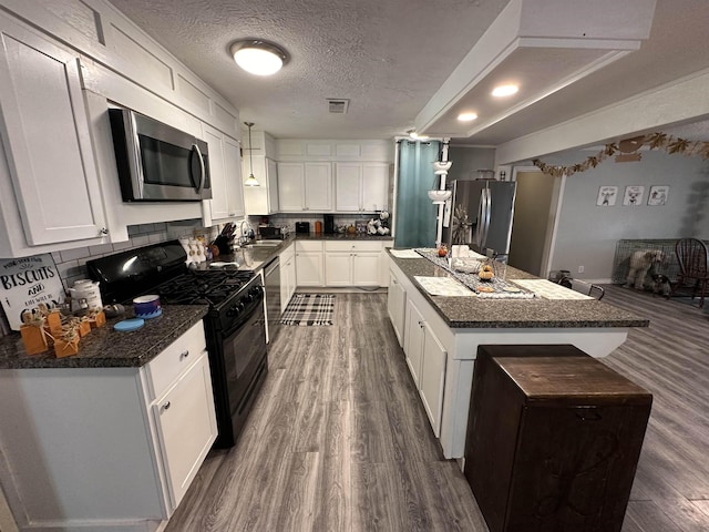 kitchen featuring white cabinetry, a center island, stainless steel appliances, dark stone countertops, and a textured ceiling