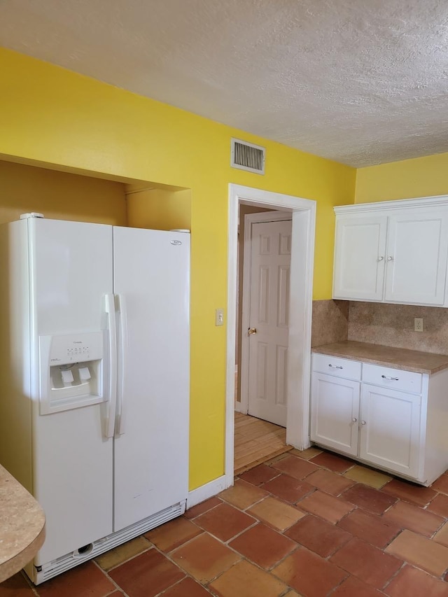 kitchen with white cabinets, white refrigerator with ice dispenser, a textured ceiling, and tasteful backsplash