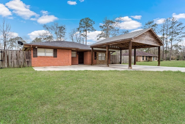 rear view of property with brick siding, a yard, concrete driveway, fence, and an attached carport