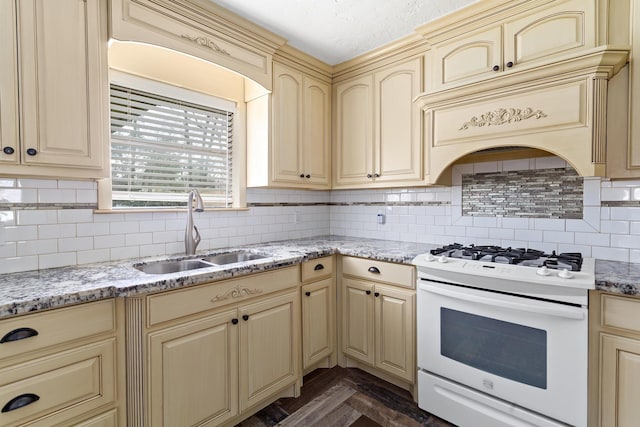 kitchen featuring cream cabinetry, a sink, decorative backsplash, and white gas range