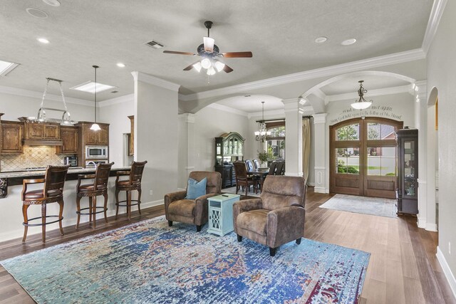 living room featuring ornate columns, ceiling fan with notable chandelier, wood-type flooring, ornamental molding, and a textured ceiling