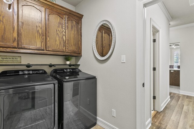 clothes washing area with crown molding, cabinets, washer and dryer, and light wood-type flooring