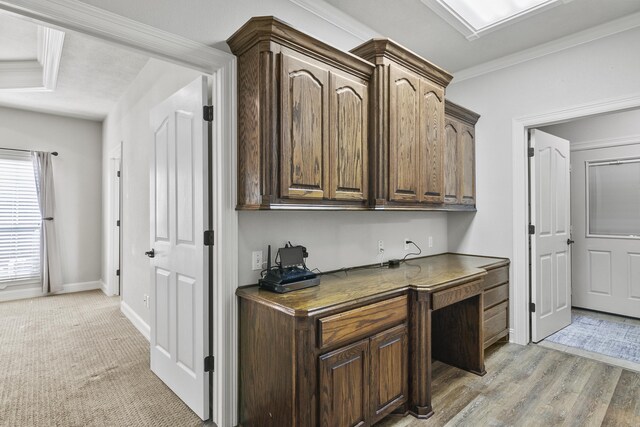 bar featuring crown molding, dark brown cabinetry, built in desk, and light hardwood / wood-style flooring