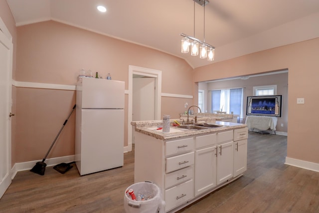 kitchen with lofted ceiling, white refrigerator, an island with sink, decorative light fixtures, and white cabinetry