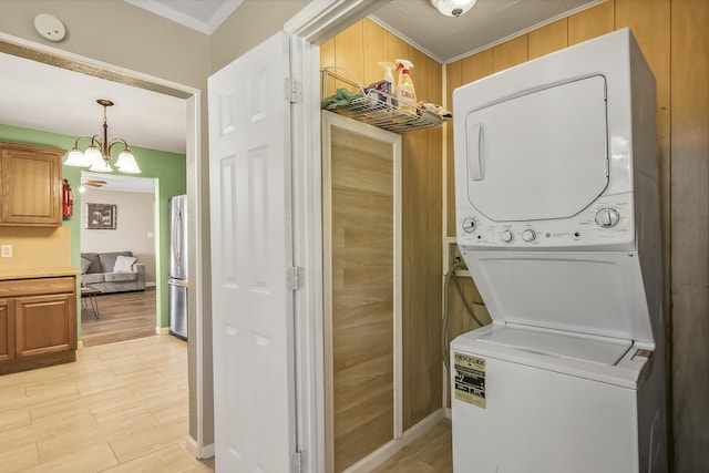 washroom featuring a notable chandelier, ornamental molding, wooden walls, and stacked washer and clothes dryer