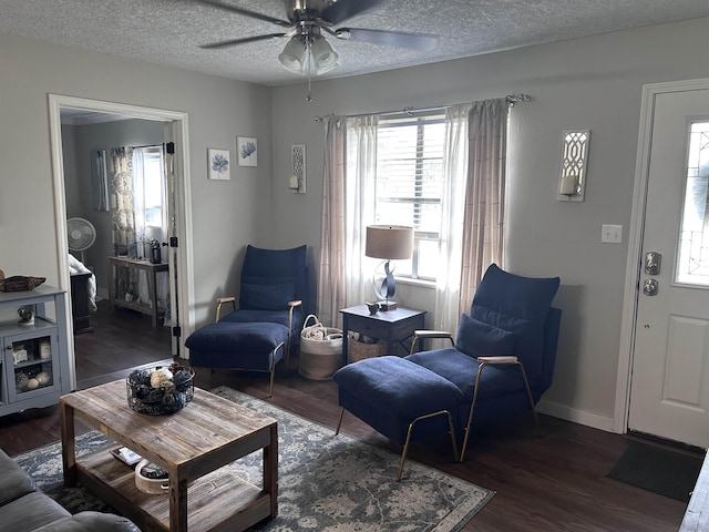 living room featuring a ceiling fan, a textured ceiling, baseboards, and wood finished floors