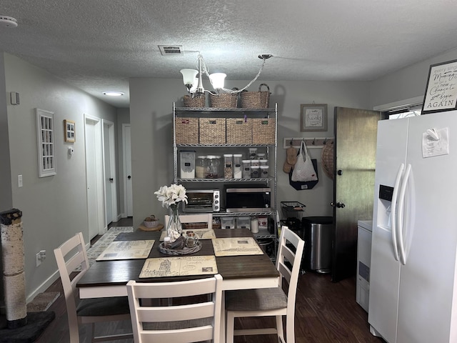 dining room featuring a textured ceiling, visible vents, a chandelier, and wood finished floors