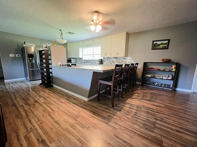 kitchen with a textured ceiling, visible vents, dark wood finished floors, ceiling fan, and stainless steel fridge with ice dispenser