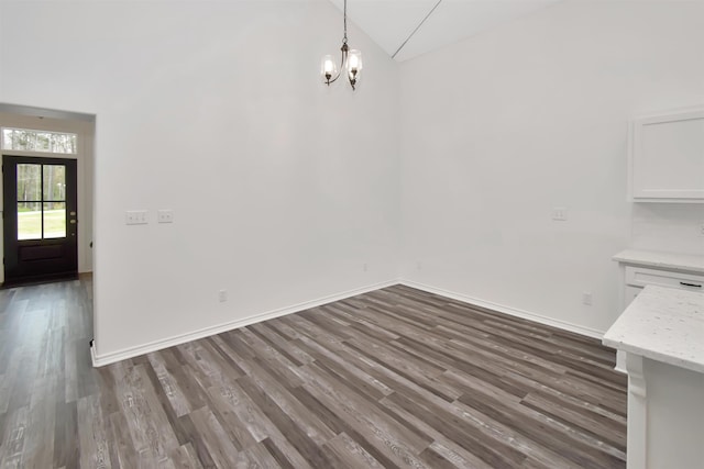 unfurnished dining area featuring baseboards, a notable chandelier, and wood finished floors