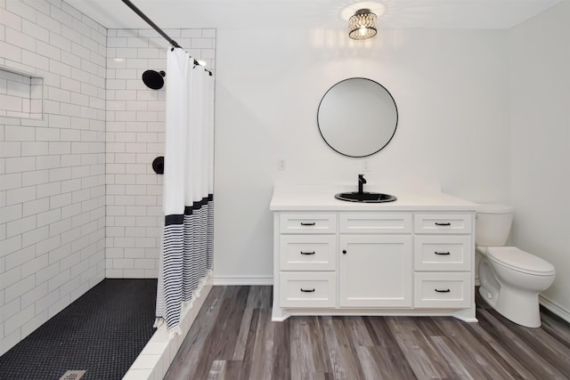 bathroom featuring toilet, wood finished floors, vanity, and a tile shower