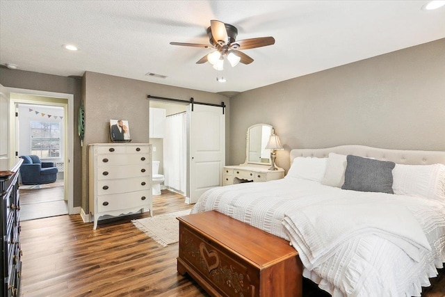 bedroom featuring dark wood-type flooring, ceiling fan, connected bathroom, and a barn door