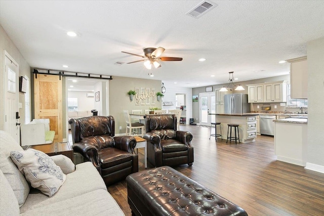 living room featuring ceiling fan, a barn door, dark hardwood / wood-style flooring, and a textured ceiling