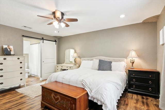 bedroom with dark wood-type flooring, ceiling fan, ensuite bathroom, and a barn door