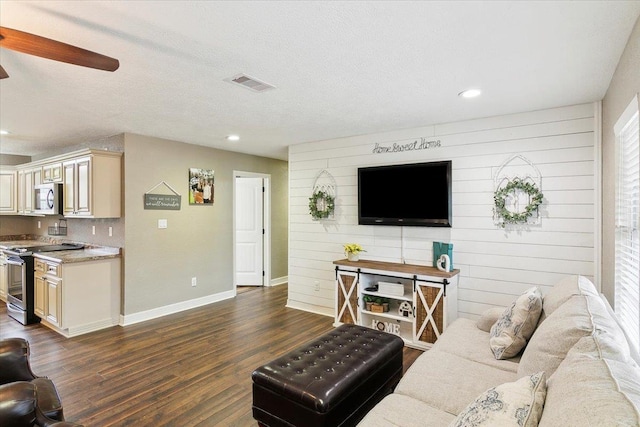 living room featuring ceiling fan, dark wood-type flooring, a textured ceiling, and wooden walls