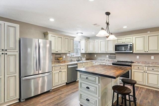 kitchen with dark wood-type flooring, butcher block counters, hanging light fixtures, stainless steel appliances, and a kitchen island