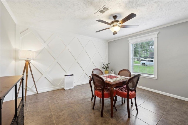 dining room featuring crown molding, visible vents, baseboards, a decorative wall, and a ceiling fan