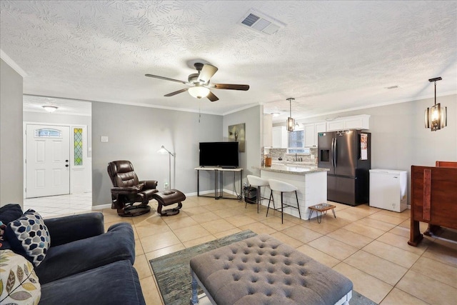 living room with light tile patterned floors, ceiling fan, crown molding, visible vents, and a textured ceiling