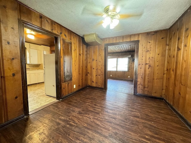 unfurnished room featuring ceiling fan, wood walls, a textured ceiling, and dark wood-type flooring