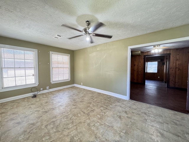 unfurnished room with ceiling fan, wood walls, and a textured ceiling