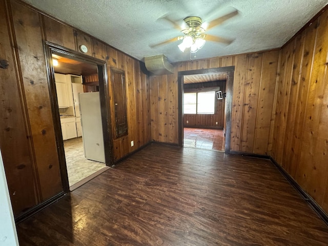 unfurnished room featuring a textured ceiling, dark hardwood / wood-style flooring, ceiling fan, and wood walls