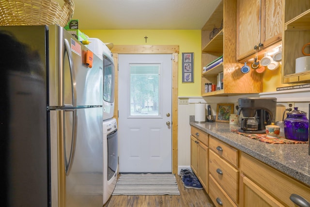 kitchen with stacked washer / dryer, stainless steel fridge, dark stone counters, and dark hardwood / wood-style floors