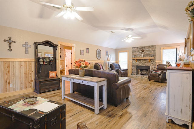 living room featuring ceiling fan, wood walls, lofted ceiling, a fireplace, and light wood-type flooring