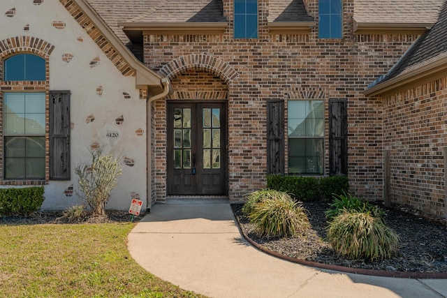 doorway to property featuring brick siding, a shingled roof, stucco siding, and french doors