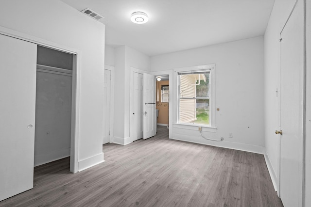 unfurnished bedroom featuring visible vents, baseboards, wood finished floors, and two closets